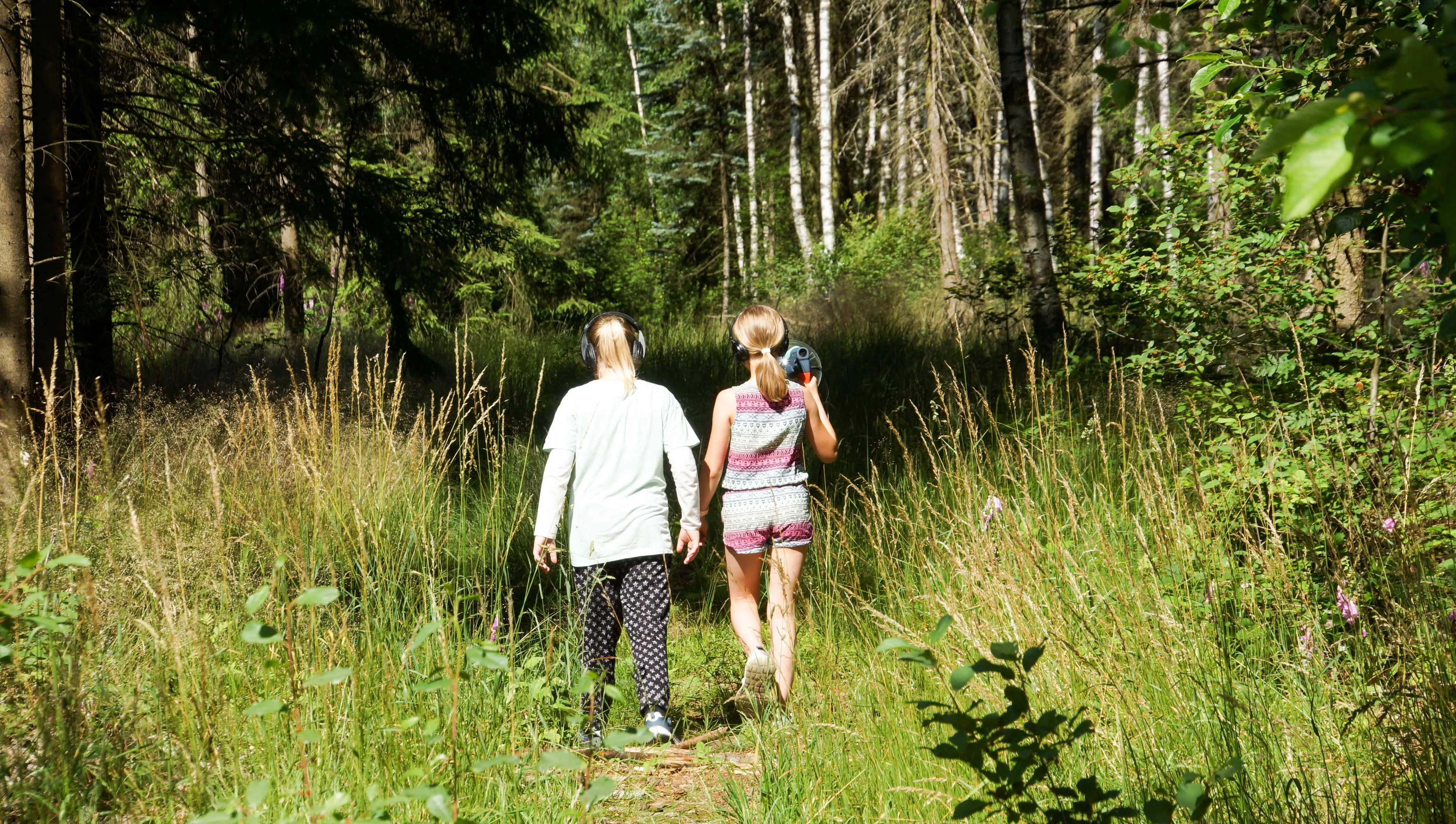 Zwei Mädchen mit Kopfhörern auf einem Waldweg
